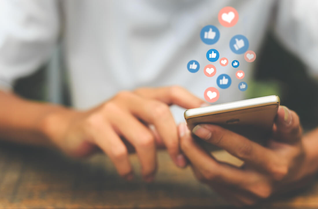 Person holding a phone with Facebook reactions floating above