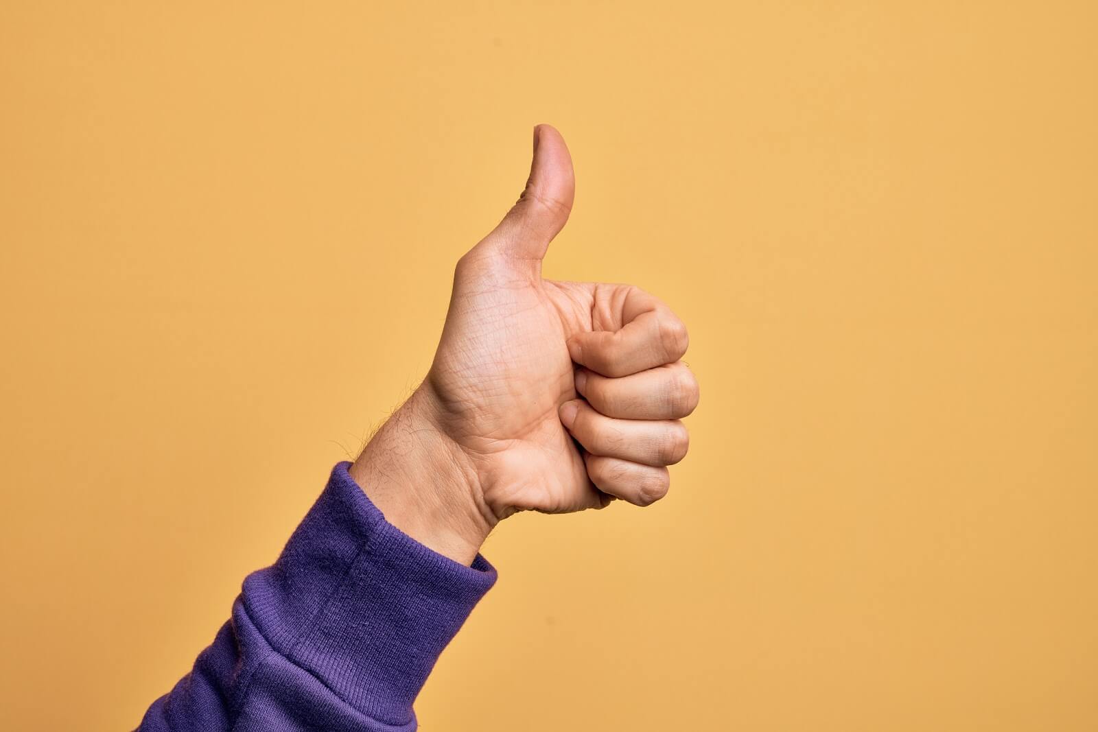 Isolated image of hand giving thumbs up on yellow background