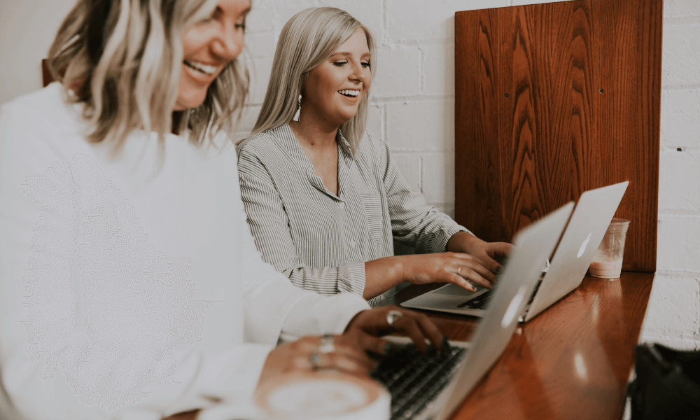 Two smiling ladies working on their laptops