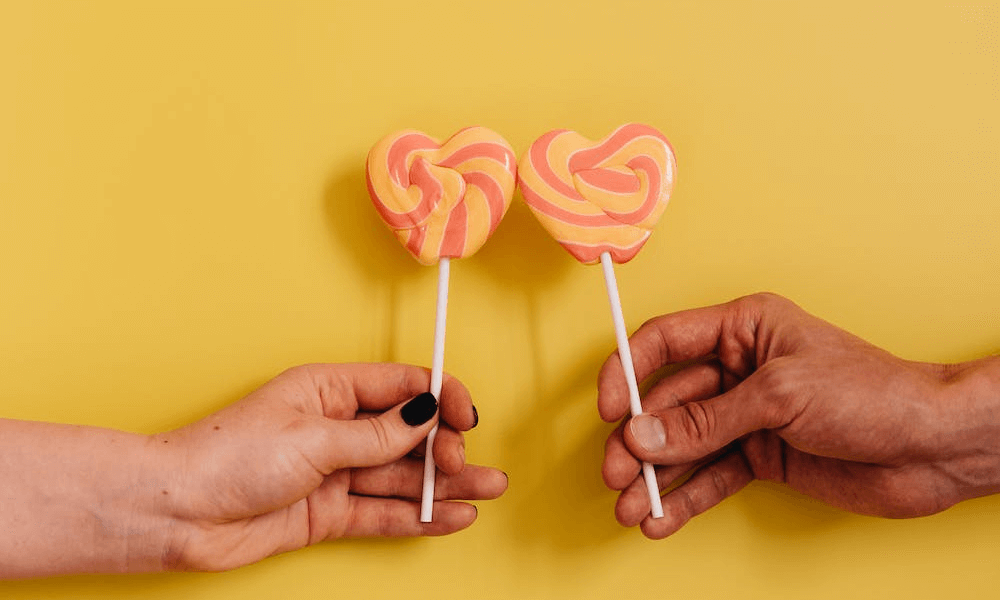 Two hands holding matching heart shaped lollipops