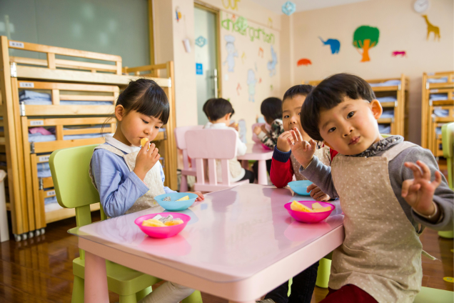 Three toddlers eating on school table