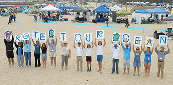 Group on a beach holding signs spelling Protect Our Ocean